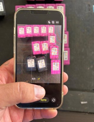 Persona fotografiando con el móvil un lote de cartuchos de tinta vacíos HP sobre una mesa
